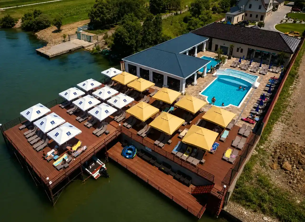 Aerial view of the riverside sun deck, umbrellas and outdoor pool at Pensiunea Elis on the Danube